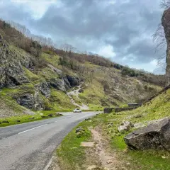 Un coche blanco toma una carretera sinuosa a través de un desfiladero verde. El camino parece ser cómo llegar a la unión de la naturaleza y la civilización.