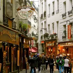 Callejuela parisina con restaurantes y gente paseando, evocando un ambiente de barrio latino en París.