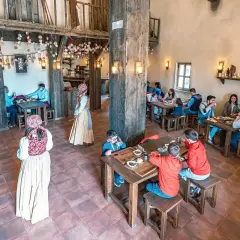 Ambiente rústico para comer en Puy du Fou. Familias y parejas disfrutan de una comida en un comedor de madera con decoración temática.