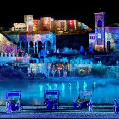 Espectáculo nocturno en Puy du Fou, Francia. Edificios históricos iluminados con proyecciones de tapices y figuras danzando en el agua.