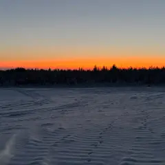 Paisaje invernal con cielo anaranjado al atardecer. Huellas en la nieve sugieren el camino para saber como ir a Laponia.