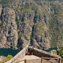 Dos excursionistas contemplan un cañón con un río azul, ideal para rutas por Galicia.