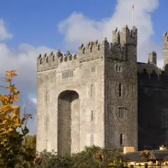 El imponente castillo de Bunratty se alza bajo un cielo azul con nubes, rodeado de follaje otoñal.