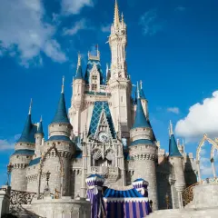 El icónico castillo de Disneyland se alza majestuoso bajo un cielo azul con nubes blancas, invitando a la magia.