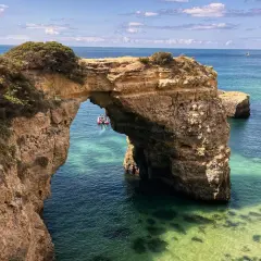 Arco natural de roca en el mar turquesa, ideal para tu plan de qué ver en Algarve en 5 días. Un bote turístico pasa por debajo.