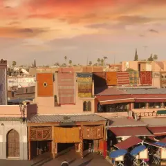 Mercado marroquí con alfombras coloridas colgadas, un minarete y tejados rojos. Consejos para viajar a Marruecos.