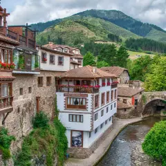 Encantadores pueblos costeros de Cantabria con casas de madera y piedra, balcones floridos y un río serpenteante bajo un puente antiguo.