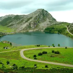 Lago en Cangas de Onís que ver: un paisaje montañoso verde con un lago sereno y carreteras serpenteantes.