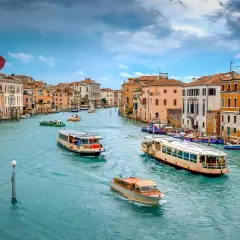 El Gran Canal de Venecia, con barcos y vaporetos, muestra cómo moverse por Venecia. Edificios coloridos flanquean el agua turquesa.