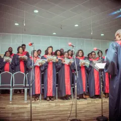 Coro cantando en una misa gospel en Nueva York, con túnicas azules y rojas, leyendo partituras.