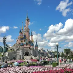 El castillo rosa de Disneyland Paris, rodeado de flores y gente, es el centro de sus atracciones.