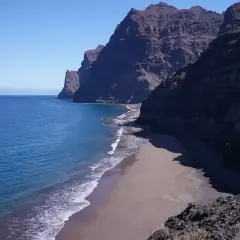 Costa salvaje con acantilados oscuros y una playa de arena dorada bañada por el mar azul. Un rincón secreto entre las mejores playas de Gran Canaria.