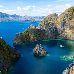 Un velero navega en aguas turquesas rodeado de acantilados verdes y rocosos en Filipinas en octubre.
