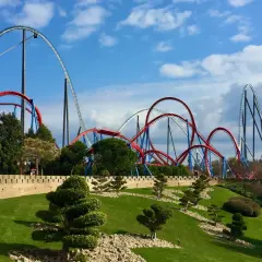 Montañas rusas rojas y azules se elevan sobre un paisaje verde y una muralla de piedra. ¡Qué ganas de ir a PortAventura!