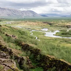 Paisaje de Thingvellir National Park con un río serpenteante, montañas al fondo y una grieta rocosa en primer plano.