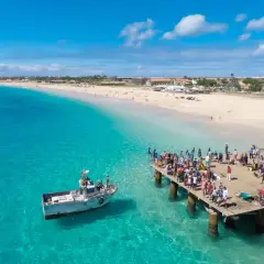 Turistas en un muelle de madera en Cabo Verde, con aguas turquesas y una playa de arena. El turismo en Cabo Verde puede ser peligroso si no se toman precauciones.