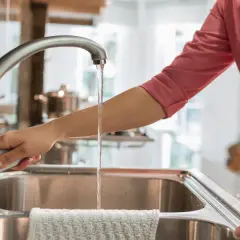 Mano abre grifo en cocina. El agua fluye, demostrando que el agua de París es potable y segura para beber.