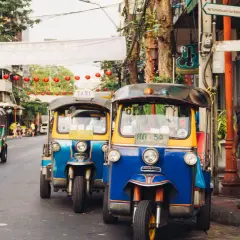 Tuk-tuks coloridos esperan en una calle de Bangkok. Un hombre observa. ¡La mejor época para viajar a Tailandia es ahora!