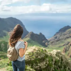 Mujer con mochila admira el paisaje montañoso y el mar, imaginando el viaje en barco Tenerife La Gomera.