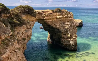 Arco natural de roca en el mar turquesa, ideal para tu plan de qué ver en Algarve en 5 días. Un bote turístico pasa por debajo.