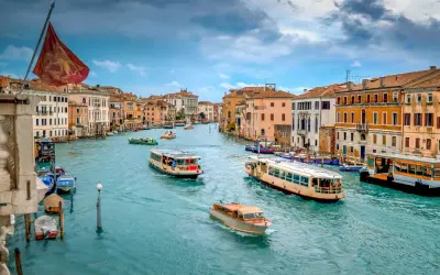 El Gran Canal de Venecia, con barcos y vaporetos, muestra cómo moverse por Venecia. Edificios coloridos flanquean el agua turquesa.