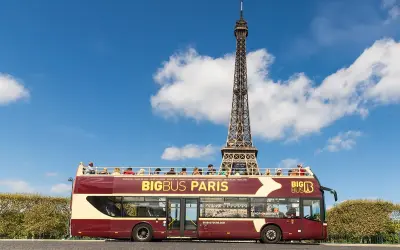 Autobús turístico Big Bus Paris con la Torre Eiffel de fondo. Turistas disfrutan del viaje en la cubierta superior.