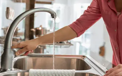 Mano abre grifo en cocina. El agua fluye, demostrando que el agua de París es potable y segura para beber.