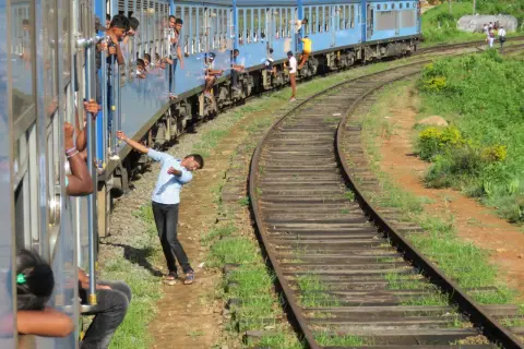 Un tren azul de Sri Lanka avanza por las vías, con pasajeros asomados a las ventanas y otros viajando en los estribos.