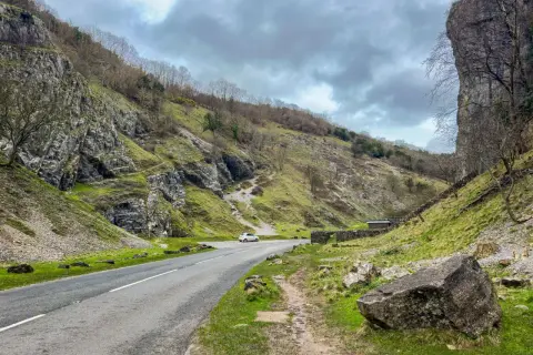 Un coche blanco toma una carretera sinuosa a través de un desfiladero verde. El camino parece ser cómo llegar a la unión de la naturaleza y la civilización.