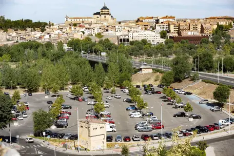 Amplio aparcamiento con muchos coches, ideal para saber donde aparcar en Toledo. Al fondo, la histórica ciudad se alza majestuosa.