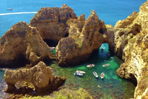 ¡Qué ganas de ir al Algarve en coche! Aquí, barcos exploran cuevas y arcos naturales en aguas cristalinas.