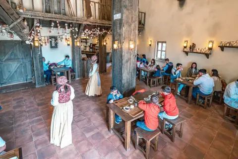 Ambiente rústico para comer en Puy du Fou. Familias y parejas disfrutan de una comida en un comedor de madera con decoración temática.