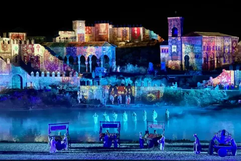 Espectáculo nocturno en Puy du Fou, Francia. Edificios históricos iluminados con proyecciones de tapices y figuras danzando en el agua.