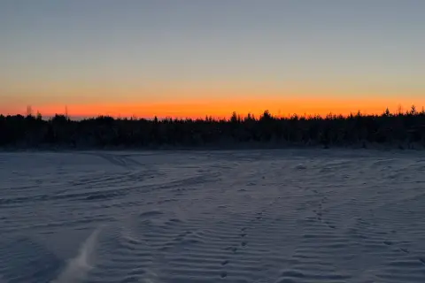 Paisaje invernal con cielo anaranjado al atardecer. Huellas en la nieve sugieren el camino para saber como ir a Laponia.
