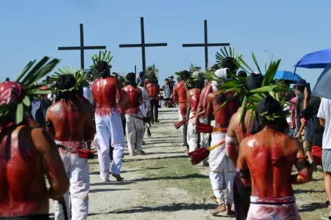 Hombres con coronas de hojas y espaldas ensangrentadas caminan hacia cruces negras, parte de una procesión de **Semana Santa Filipinas**.