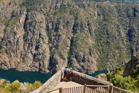 Dos excursionistas contemplan un cañón con un río azul, ideal para rutas por Galicia.