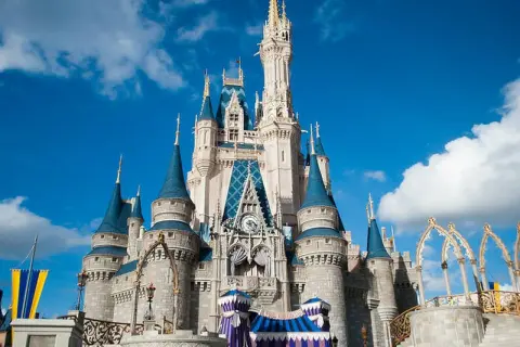 El icónico castillo de Disneyland se alza majestuoso bajo un cielo azul con nubes blancas, invitando a la magia.