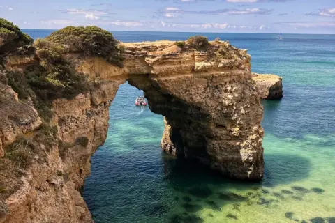 Arco natural de roca en el mar turquesa, ideal para tu plan de qué ver en Algarve en 5 días. Un bote turístico pasa por debajo.