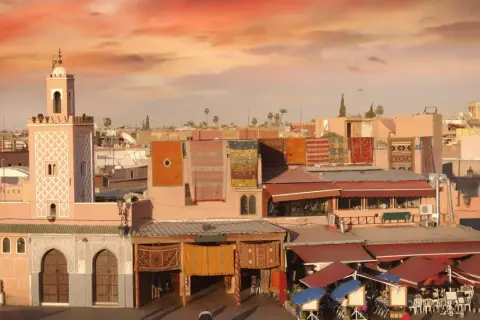 Mercado marroquí con alfombras coloridas colgadas, un minarete y tejados rojos. Consejos para viajar a Marruecos.