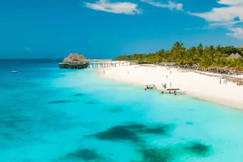 Playa paradisíaca en Tanzania en agosto. Aguas turquesas, arena blanca, palmeras y un muelle con un restaurante.