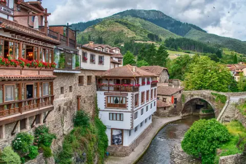 Encantadores pueblos costeros de Cantabria con casas de madera y piedra, balcones floridos y un río serpenteante bajo un puente antiguo.