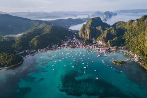 Vista aérea de El Nido, Filipinas. Un mar turquesa lleno de barcos, con una costa verde y montañosa. ¡Perfecto para tu próxima aventura con una tarjeta SIM Filipinas!