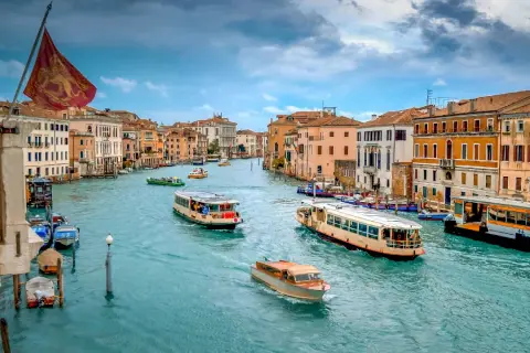 El Gran Canal de Venecia, con barcos y vaporetos, muestra cómo moverse por Venecia. Edificios coloridos flanquean el agua turquesa.