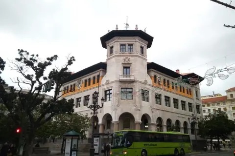 Autobús verde de ALSA en la calle, frente a un edificio histórico. Un buen lugar para aparcar en Santander y disfrutar de la arquitectura.