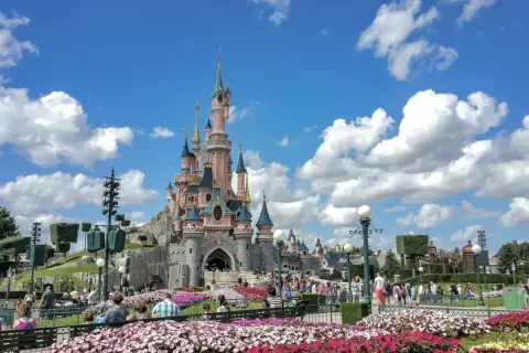 El castillo rosa de Disneyland Paris, rodeado de flores y gente, es el centro de sus atracciones.