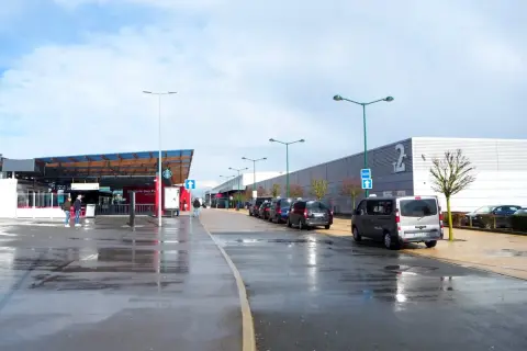 Llegando a **París Beauvais al centro**, taxis esperan bajo un cielo nublado. El aeropuerto tiene una zona de embarque y un edificio largo con el número 2.