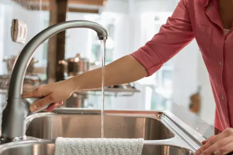 Mano abre grifo en cocina. El agua fluye, demostrando que el agua de París es potable y segura para beber.