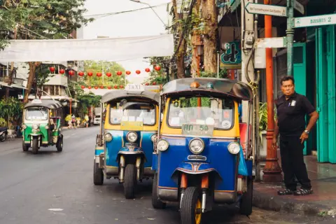 Tuk-tuks coloridos esperan en una calle de Bangkok. Un hombre observa. ¡La mejor época para viajar a Tailandia es ahora!