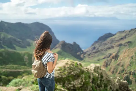 Mujer con mochila admira el paisaje montañoso y el mar, imaginando el viaje en barco Tenerife La Gomera.