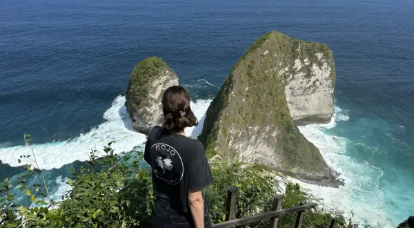 Una mujer admira el paisaje de acantilados verdes y mar turquesa, un momento de su viaje a Indonesia de 15 días.